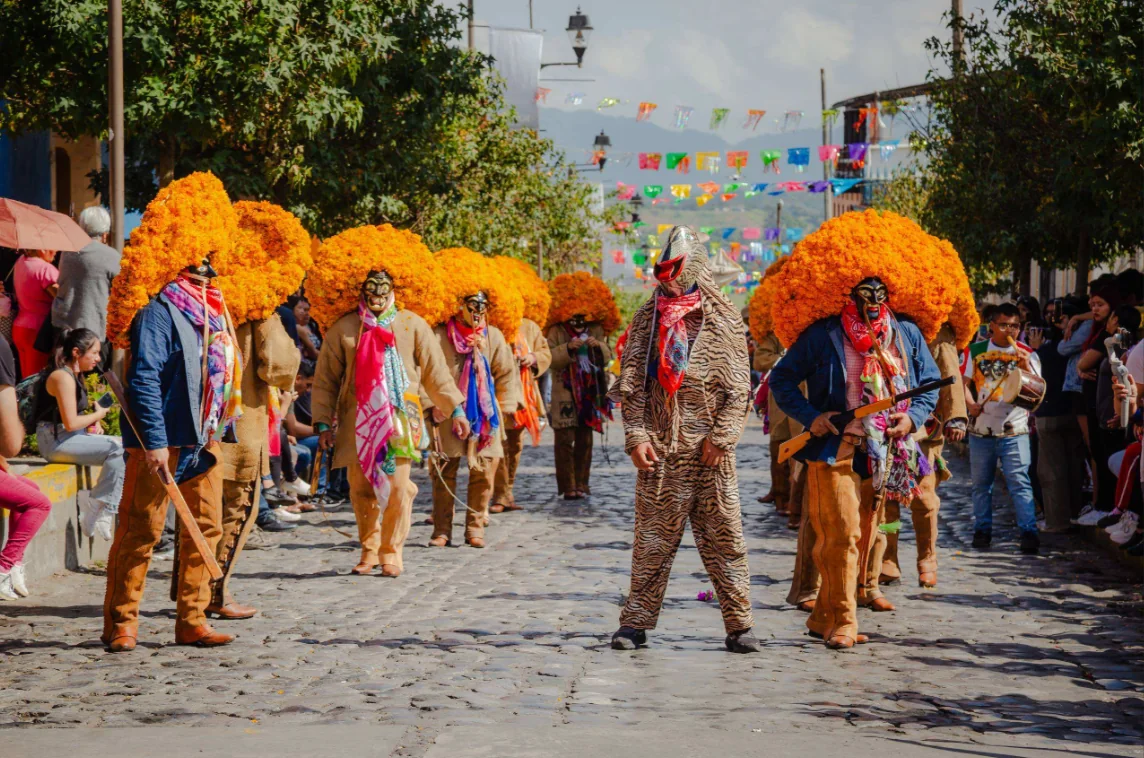 Comparsa de máscaras danzantes recorriendo una calle durante el festival
